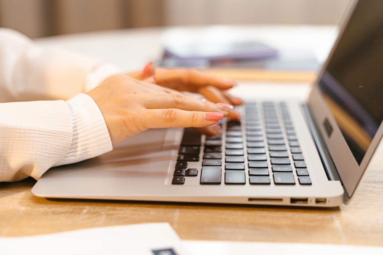 Person writing on laptop computer with notes and documents on desk