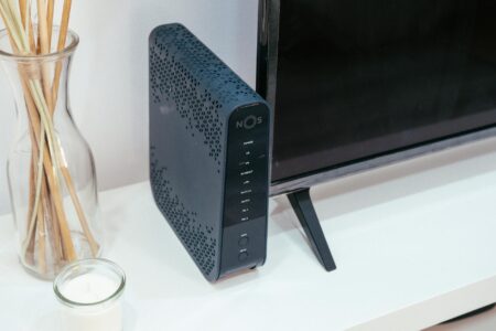 A smart home hub device sitting on a desk next to a smartphone displaying a home control app